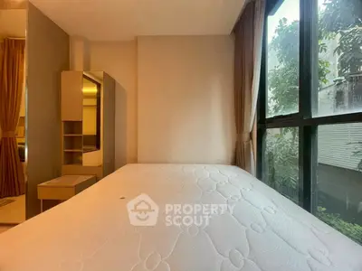 Cozy bedroom with large window and natural light, featuring a comfortable mattress and elegant curtains.