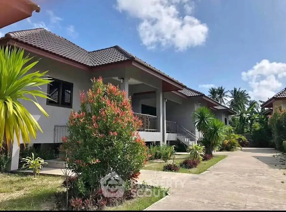Charming tropical bungalow with lush garden and spacious driveway under clear blue skies.