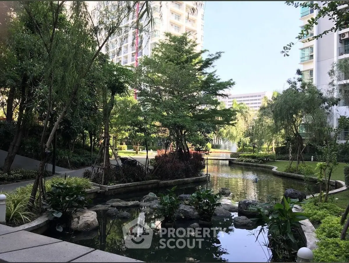 Serene garden view with lush greenery and tranquil pond in modern residential complex.