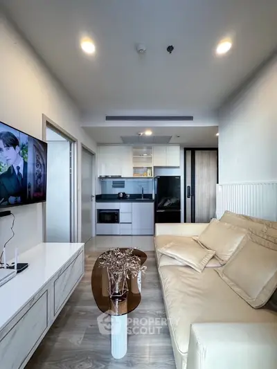 Modern living room with open kitchen, beige sofa, and wall-mounted TV in a stylish apartment.