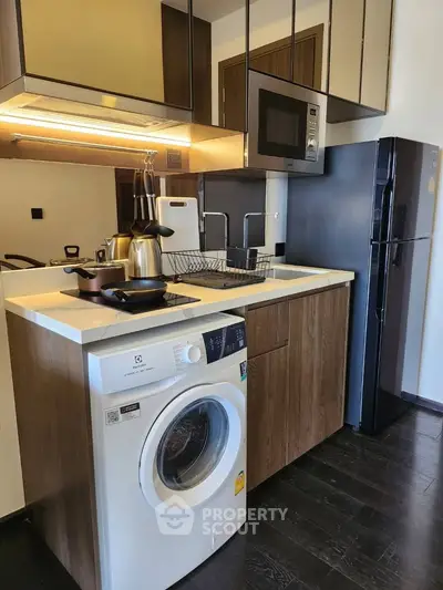 Modern kitchen with sleek appliances including washing machine and fridge, dark wood cabinetry, and stylish lighting.