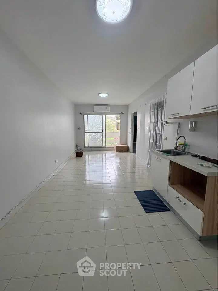 Spacious open-plan living area with modern kitchen and large window for natural light.