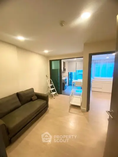 Modern living room with cozy sofa and open kitchen layout, featuring bright lighting and sleek design.