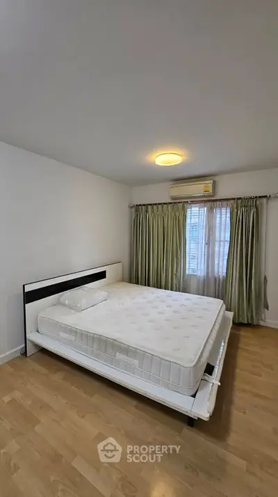 Spacious bedroom with large bed and natural light, featuring elegant curtains and wooden flooring.