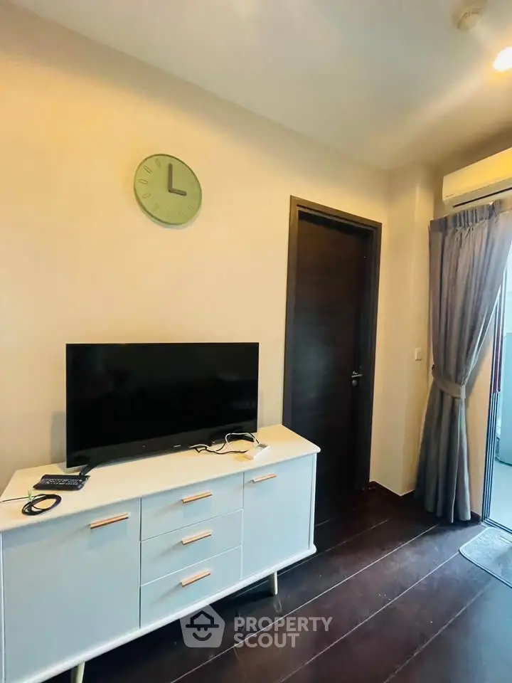 Modern living room with sleek TV stand and wall clock, featuring elegant dark flooring and a cozy ambiance.