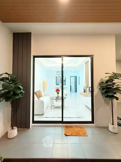 Modern living room view through sliding glass doors with stylish decor and indoor plants.