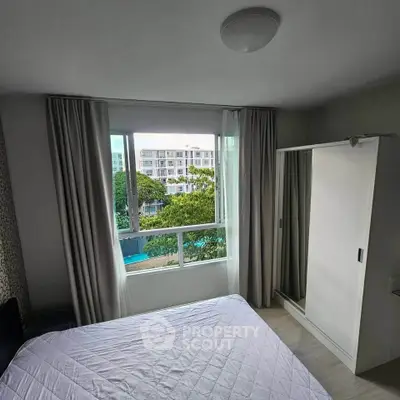 Cozy bedroom with large window offering a serene view of greenery and modern buildings.