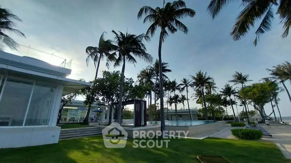 Luxurious beachfront property with palm trees and modern architecture, offering serene ocean views and lush green surroundings.