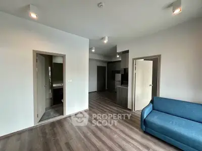 Modern living room with sleek flooring and cozy blue sofa, adjacent to kitchen and bathroom.