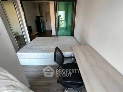Compact bedroom with bed, desk, and chair, featuring modern sliding glass doors and wooden flooring.