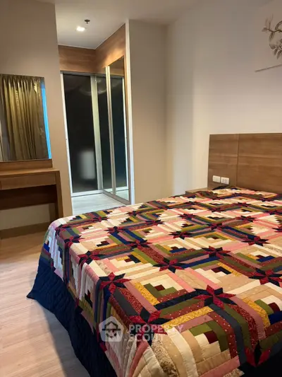Cozy bedroom with colorful quilt and modern wooden furniture, featuring a walk-in closet.