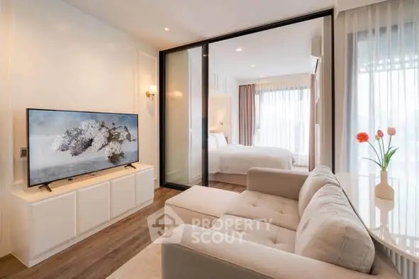 Modern living room with cozy sofa and large TV, adjacent to a bright bedroom with natural light.