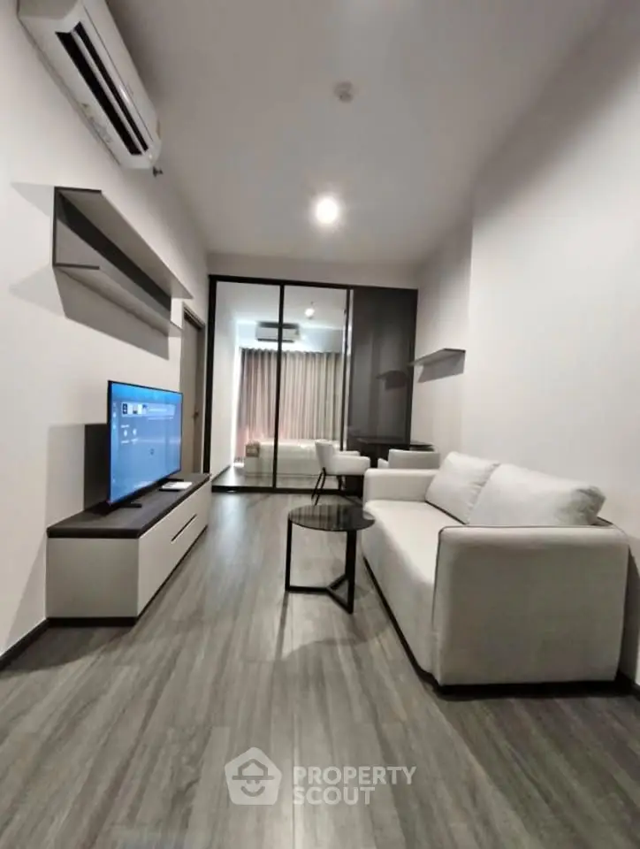 Modern living room with sleek design, featuring a white sofa, flat-screen TV, and air conditioning, perfect for urban living.
