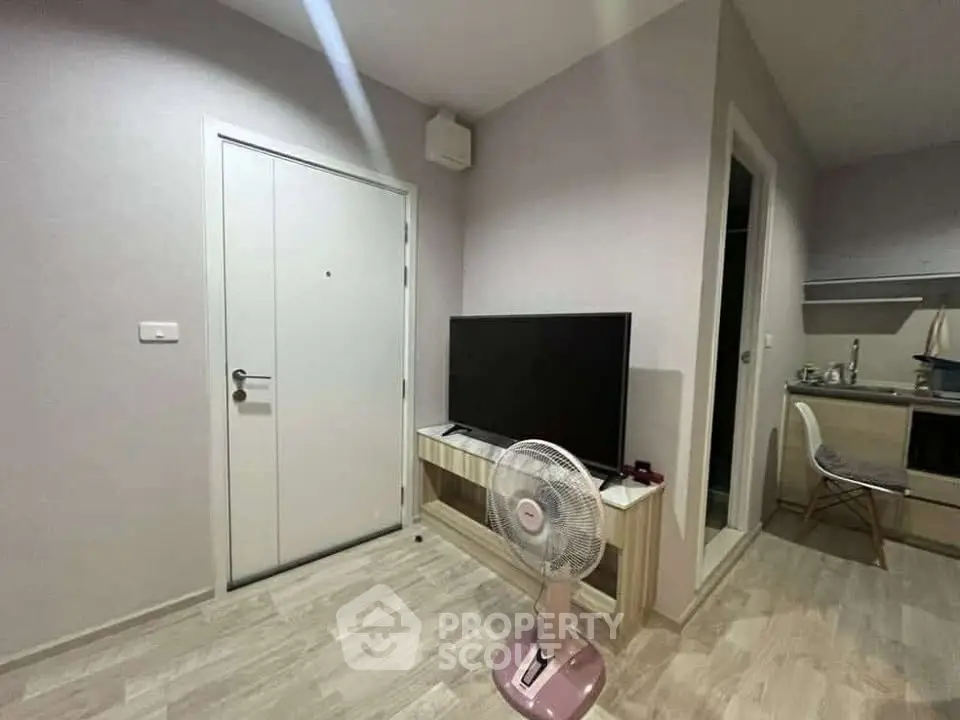Modern apartment interior with TV, fan, and kitchen area, showcasing sleek design and functionality.