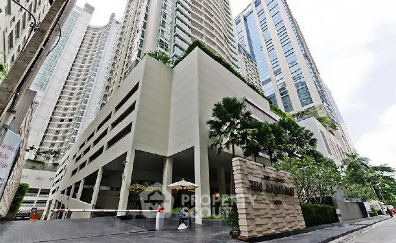 Luxurious high-rise condominium entrance with modern architecture and lush greenery in urban setting.