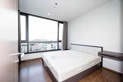 Spacious bedroom with large window offering city views, featuring a modern bed and wooden flooring.