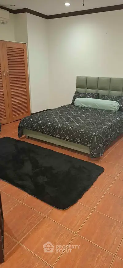 Spacious bedroom with modern decor and wooden flooring, featuring a stylish bed and cozy rug.