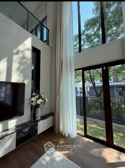 Luxurious living room with high ceilings and large windows offering a stunning garden view.