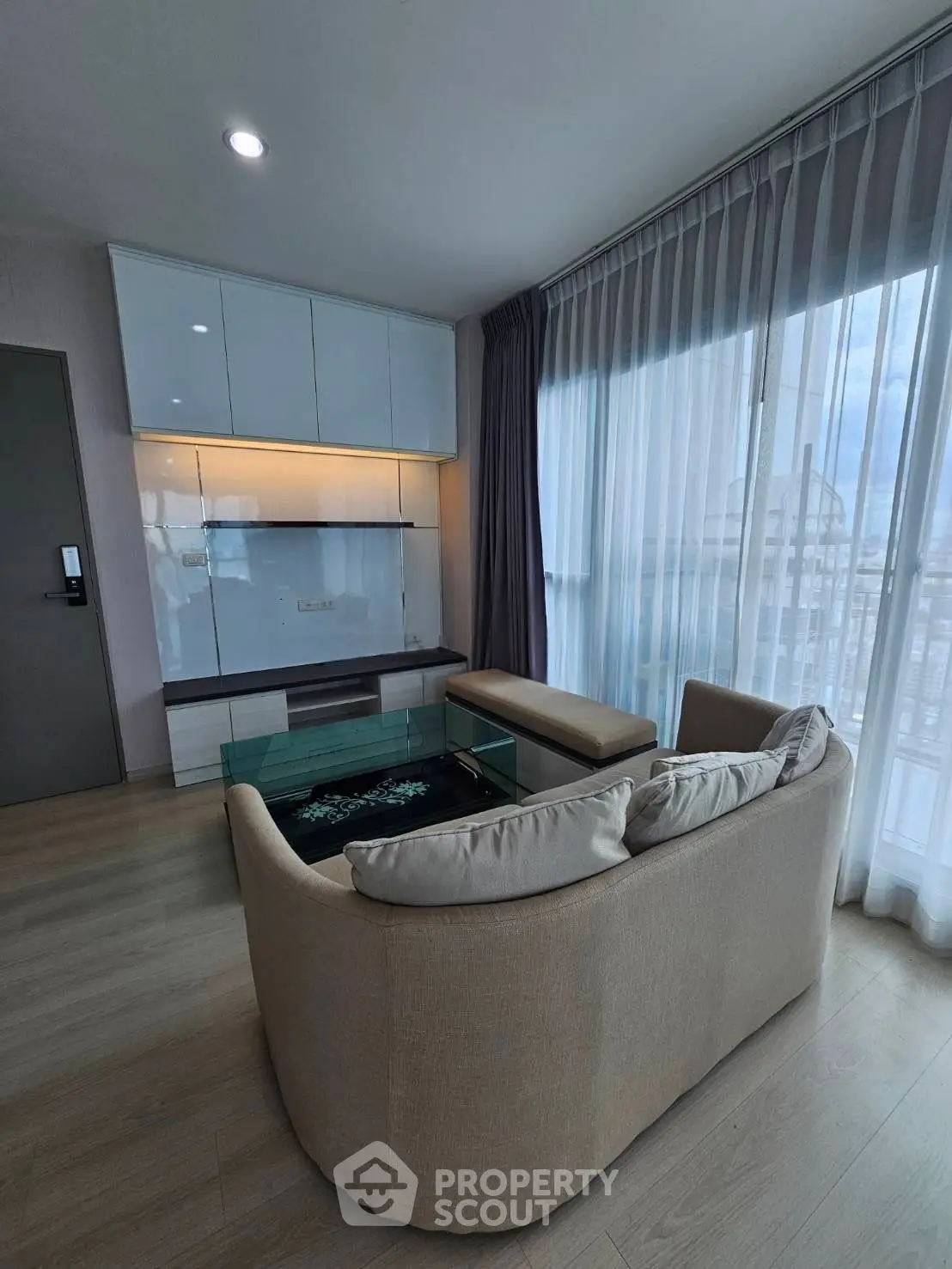 Modern living room with elegant sofa and glass coffee table, featuring floor-to-ceiling windows and stylish decor.