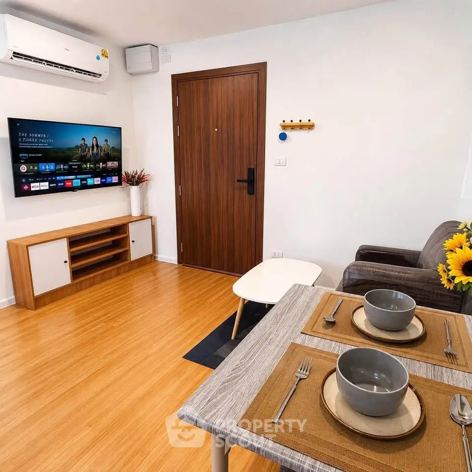 Modern living room with TV, cozy seating, and dining area in stylish apartment.