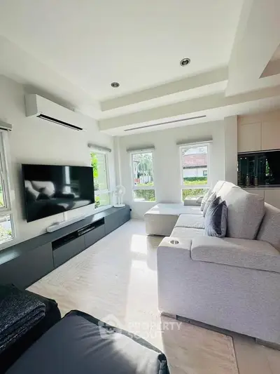 Modern living room with large windows, sleek furniture, and a wall-mounted TV, offering a bright and airy ambiance.
