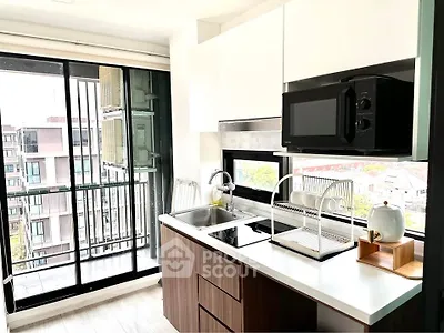 Modern kitchen with sleek cabinetry and balcony view, featuring a microwave and dish rack.
