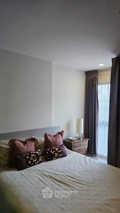 Cozy bedroom with stylish decor and natural light from large window.