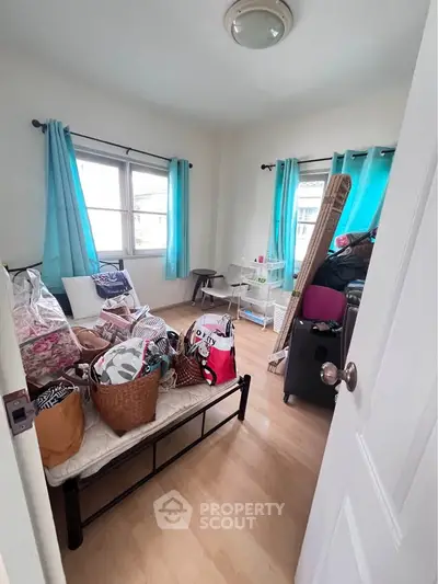 Cozy bedroom with natural light, featuring wooden flooring and vibrant blue curtains, ideal for personal retreat.