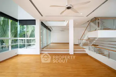Spacious modern living room with wooden floors and large windows offering lush garden views.