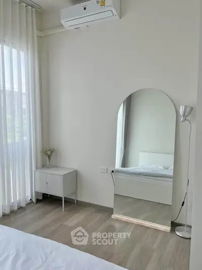 Bright bedroom with modern decor, featuring a large mirror, air conditioning, and natural light from sheer curtains.
