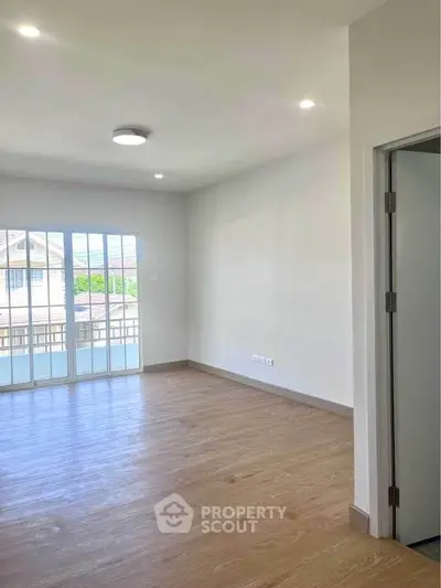 Spacious empty room with wooden flooring and large windows offering natural light.