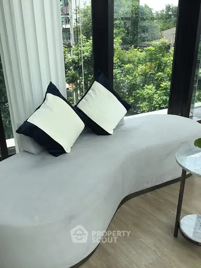 Modern living room with stylish curved sofa and large windows overlooking greenery.