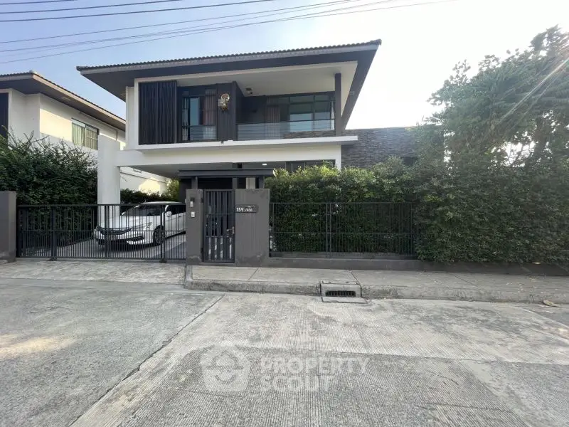 Modern two-story house with sleek design and gated driveway in suburban neighborhood.