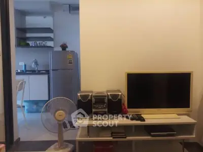 Cozy living room with TV and fan, adjacent to a modern kitchen with fridge.