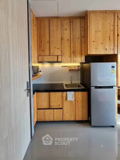 Modern kitchen with wooden cabinets and stainless steel fridge in a compact layout.
