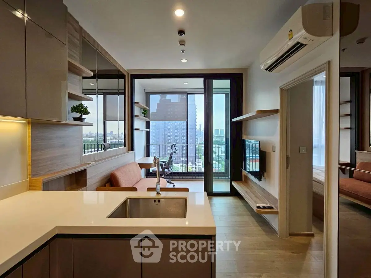 Modern open-plan kitchen and living area with balcony view in urban apartment.