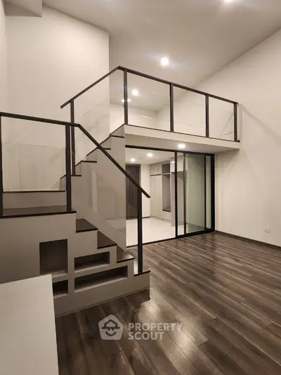 Modern loft apartment with sleek staircase and glass railing, featuring high ceilings and elegant wooden flooring.