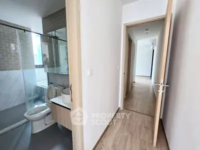 Modern apartment hallway with bathroom featuring glass shower and sleek fixtures.