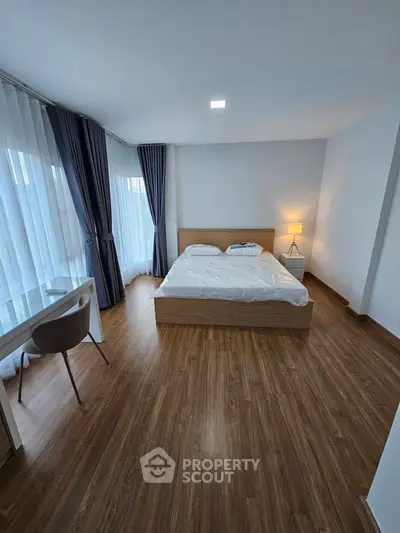 Spacious bedroom with wooden flooring, large windows, and modern furnishings.
