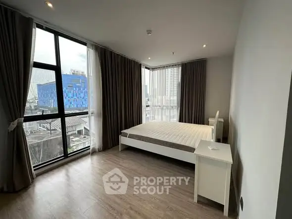 Modern bedroom with large windows and city view, featuring minimalist decor and natural light.