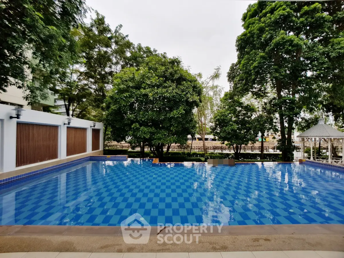 Luxurious outdoor swimming pool surrounded by lush greenery in a serene residential complex.