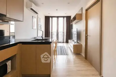 Modern apartment interior with open kitchen and cozy living area, featuring sleek wooden cabinetry and natural light.