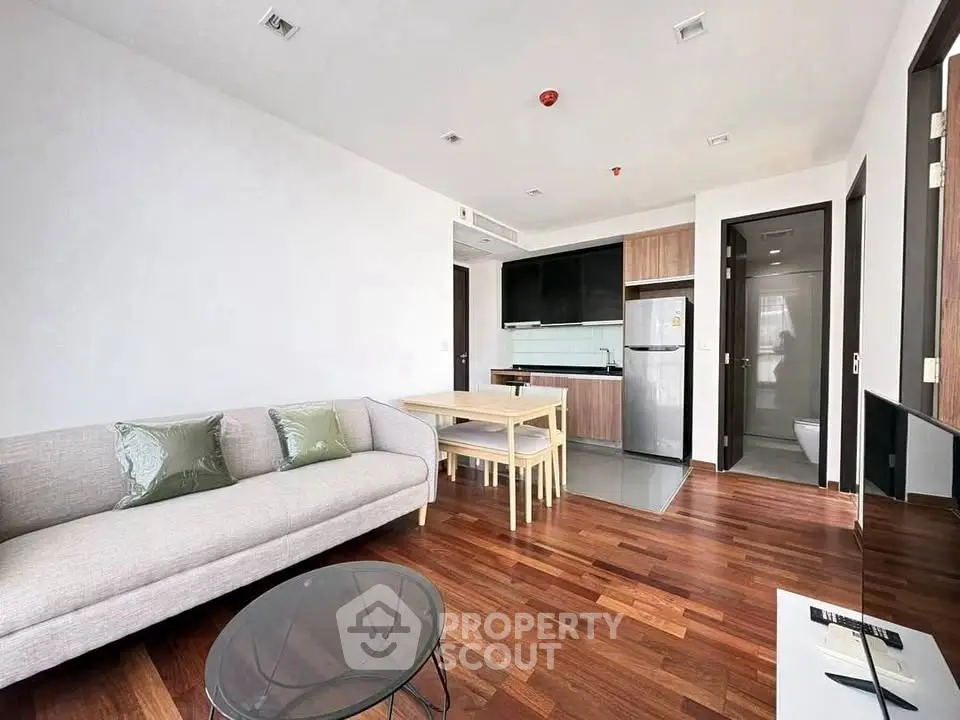 Modern living room with open kitchen, wooden flooring, and stylish furniture in a contemporary apartment.