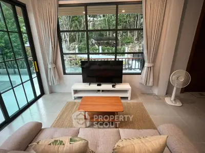 Charming living room with large windows and garden view, featuring cozy seating and modern decor.
