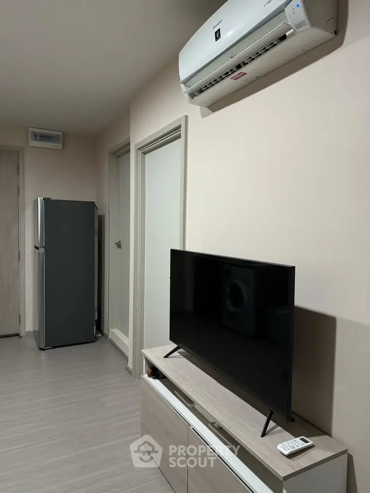 Modern living room with sleek TV, air conditioning, and refrigerator in a stylish apartment.