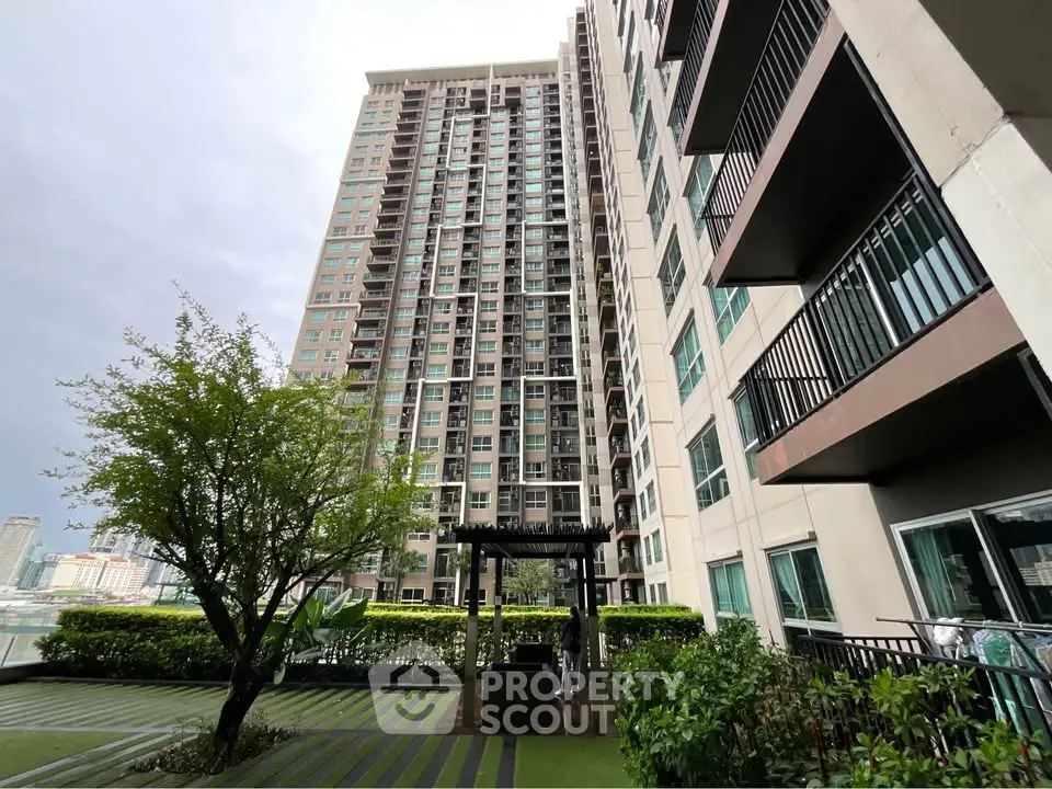 Modern high-rise building with lush greenery and outdoor seating area.