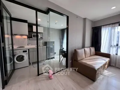 Modern living room with glass partition, washing machine, and cozy sofa in bright apartment.