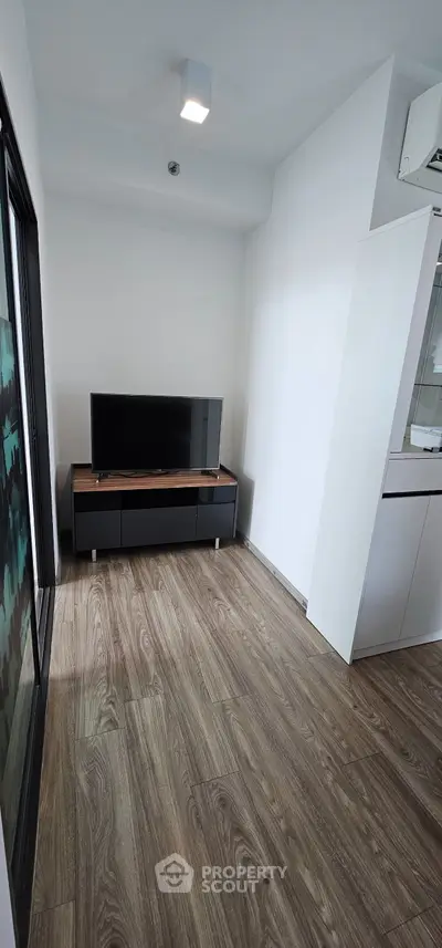 Modern compact living room with sleek wooden flooring and minimalist TV setup.