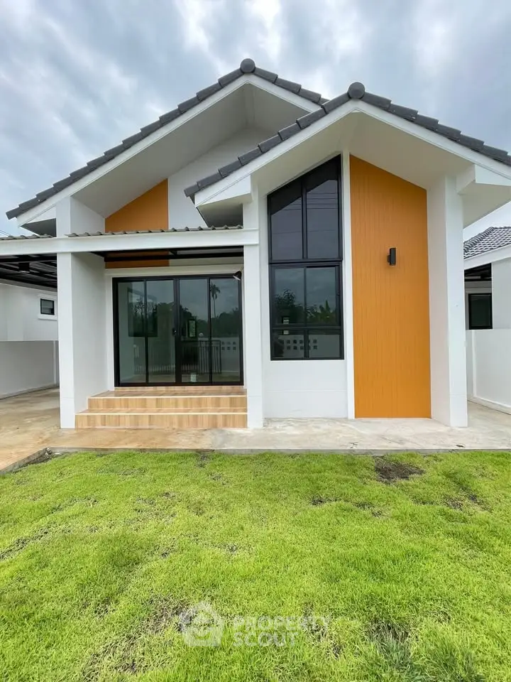 Modern single-story house with large windows and lush green lawn, showcasing contemporary architecture and inviting entrance.