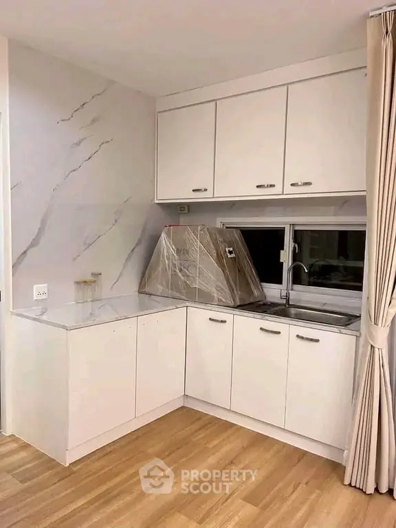 Modern kitchen with sleek white cabinets and marble backsplash in a cozy apartment.